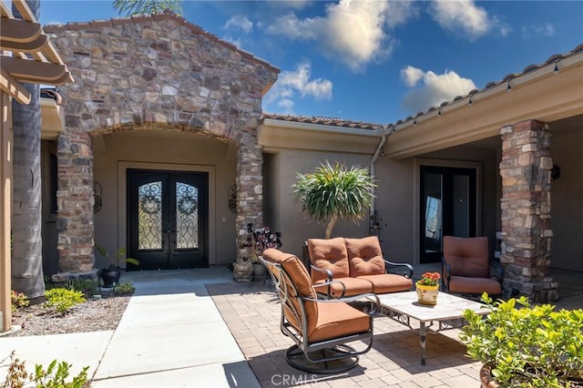 view of exterior entry featuring a patio, stucco siding, french doors, an outdoor living space, and a tile roof
