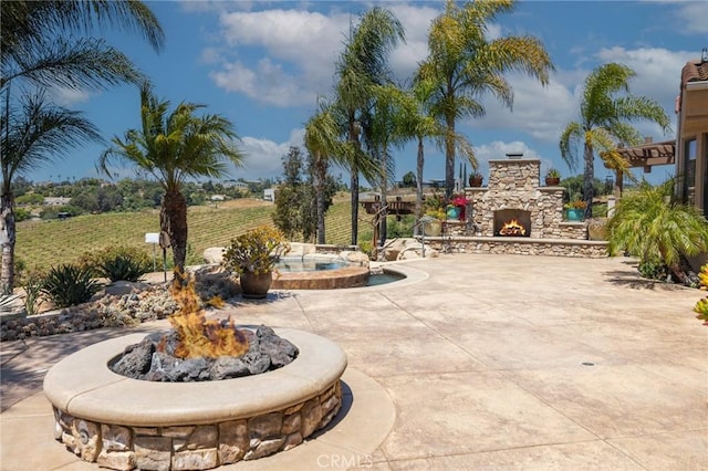 view of patio with an outdoor stone fireplace and an in ground hot tub