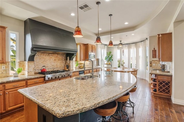 kitchen with visible vents, a kitchen island with sink, wall chimney range hood, a sink, and appliances with stainless steel finishes