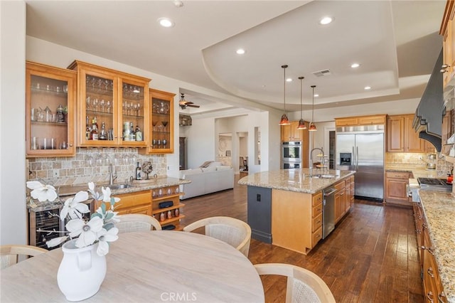 kitchen featuring a sink, dark wood finished floors, stainless steel appliances, decorative backsplash, and a center island with sink