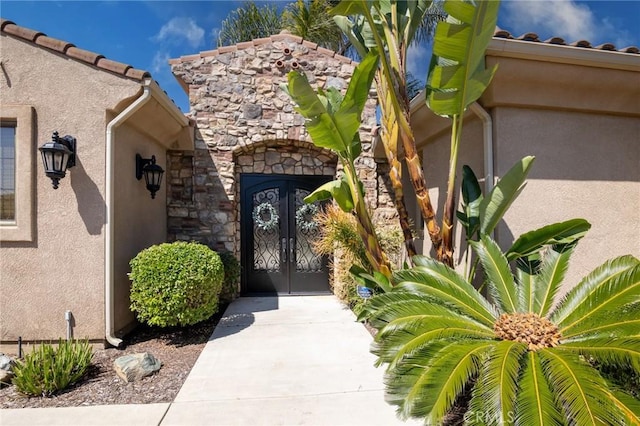 doorway to property featuring french doors, stucco siding, and stone siding