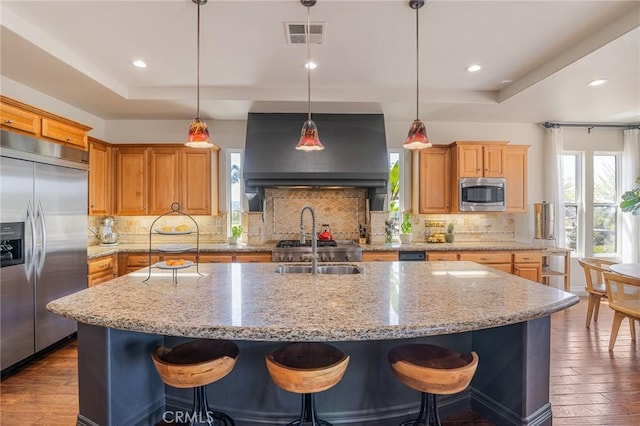kitchen featuring a raised ceiling, built in appliances, dark wood finished floors, and ventilation hood