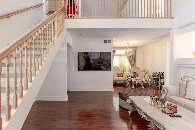 living area with visible vents, a towering ceiling, wood finished floors, baseboards, and a notable chandelier