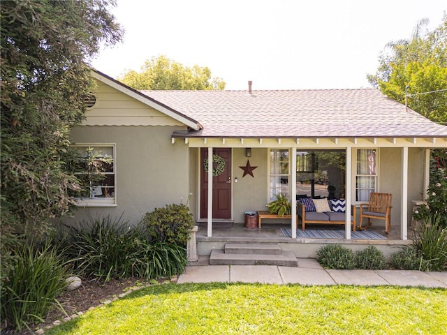 entrance to property featuring a shingled roof, stucco siding, and a yard