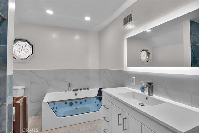 bathroom with vanity, recessed lighting, tile walls, a tub with jets, and visible vents