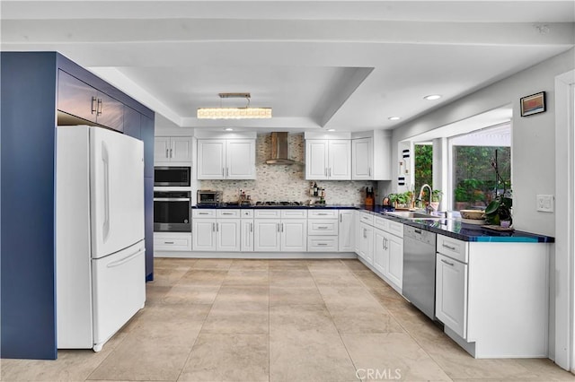 kitchen featuring dark countertops, a sink, a raised ceiling, stainless steel appliances, and wall chimney exhaust hood