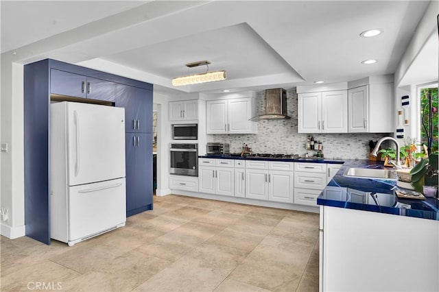 kitchen featuring wall chimney exhaust hood, a tray ceiling, a sink, backsplash, and stainless steel appliances