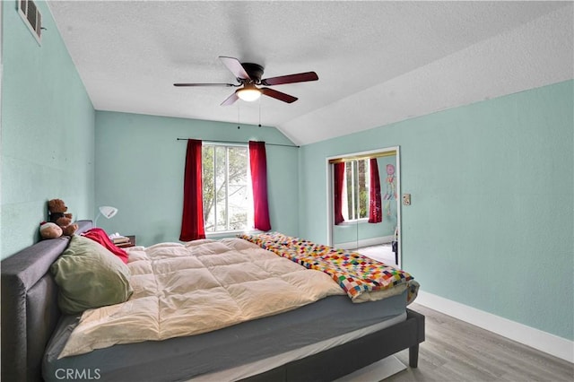 bedroom featuring visible vents, wood finished floors, baseboards, a textured ceiling, and vaulted ceiling