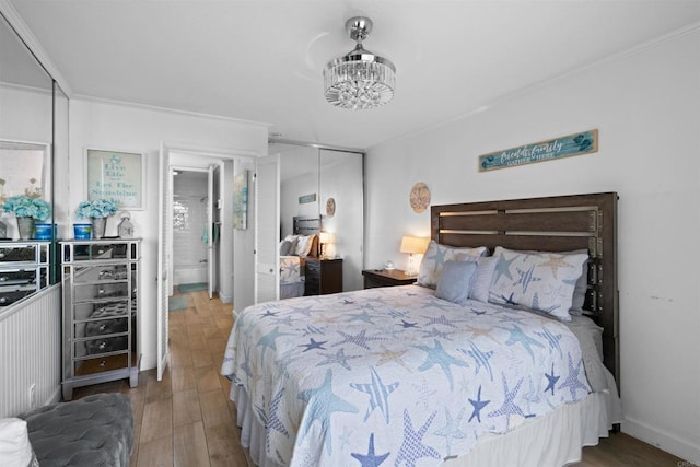 bedroom with an inviting chandelier, crown molding, wood finished floors, and a closet