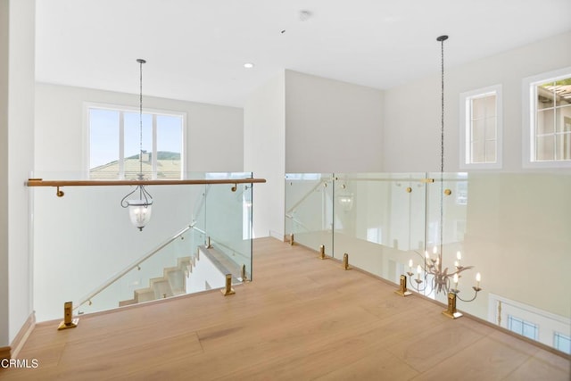 corridor with wood finished floors, a chandelier, and an upstairs landing