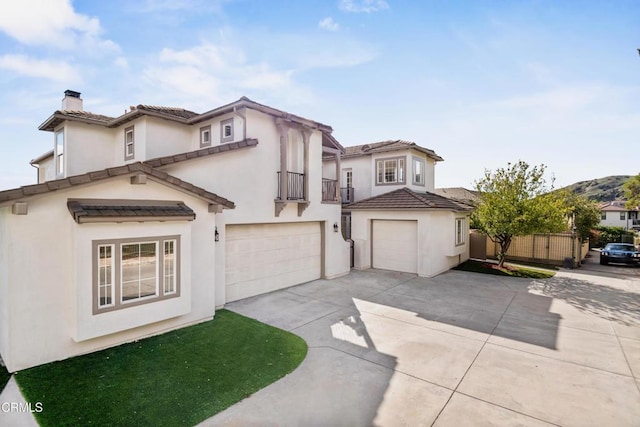 mediterranean / spanish home featuring a garage, stucco siding, a chimney, a balcony, and driveway