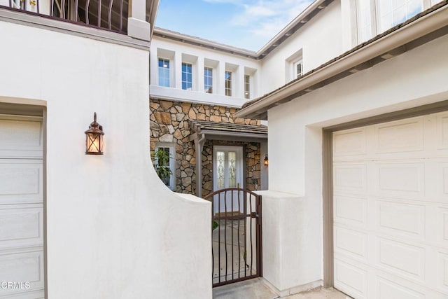 property entrance with a garage, stucco siding, and stone siding