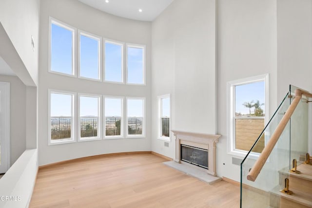 unfurnished living room with wood finished floors, baseboards, a glass covered fireplace, and a high ceiling