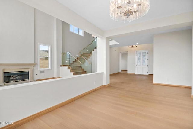 unfurnished living room with a chandelier, a glass covered fireplace, stairs, baseboards, and wood finished floors