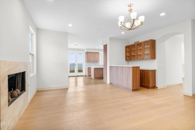 unfurnished living room featuring an inviting chandelier, a fireplace, recessed lighting, arched walkways, and light wood-style flooring