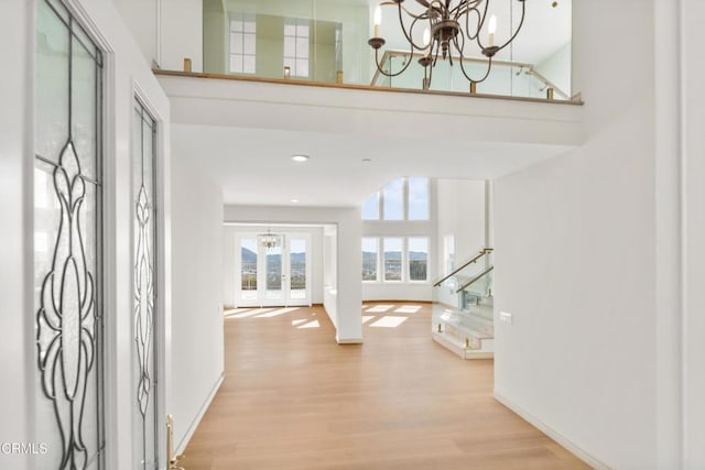 foyer with an inviting chandelier, baseboards, a towering ceiling, and wood finished floors