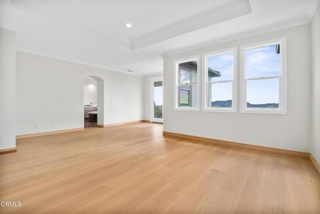 unfurnished room with a raised ceiling, arched walkways, crown molding, and light wood finished floors