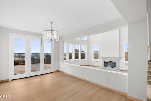 unfurnished living room with light wood-type flooring, a glass covered fireplace, a chandelier, and a healthy amount of sunlight