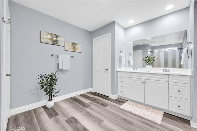bathroom featuring wood finished floors, baseboards, double vanity, and recessed lighting