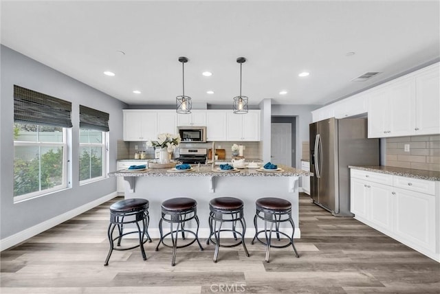 kitchen featuring stainless steel appliances, decorative backsplash, white cabinetry, light wood-style floors, and recessed lighting