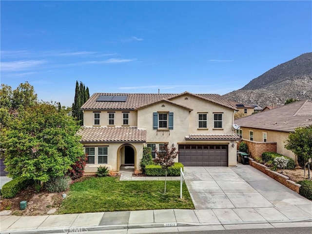 mediterranean / spanish house with stucco siding, concrete driveway, an attached garage, solar panels, and a front yard