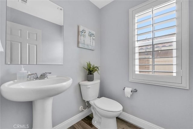 half bathroom featuring baseboards, toilet, wood finished floors, and a sink