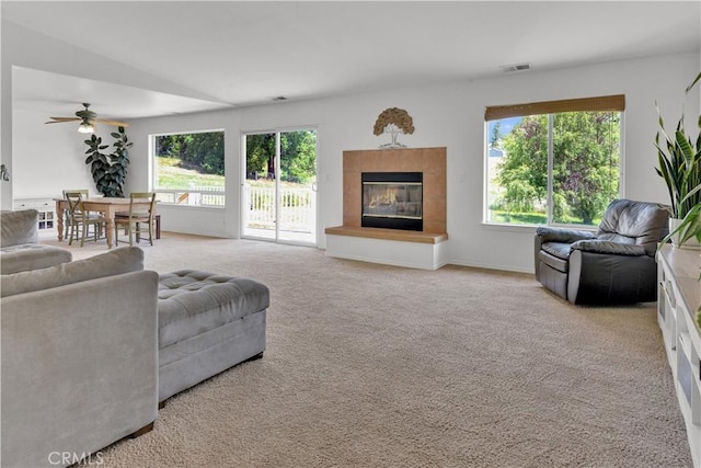 living room with a tiled fireplace, visible vents, a ceiling fan, and a wealth of natural light