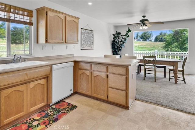 kitchen featuring a peninsula, white dishwasher, ceiling fan, light countertops, and a sink