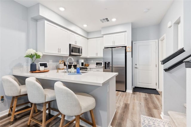 kitchen featuring stainless steel appliances, a peninsula, a kitchen bar, a sink, and recessed lighting