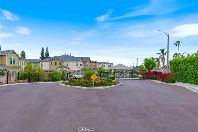 view of asphalt road with a residential view, street lighting, curbs, and a gated entry
