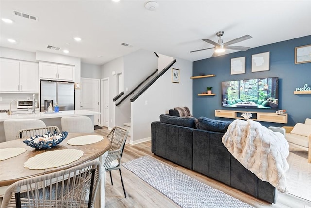 living room featuring a ceiling fan, light wood-style floors, stairs, recessed lighting, and baseboards
