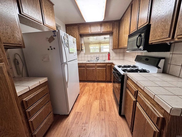kitchen featuring backsplash, tile countertops, a sink, black appliances, and light wood-style floors