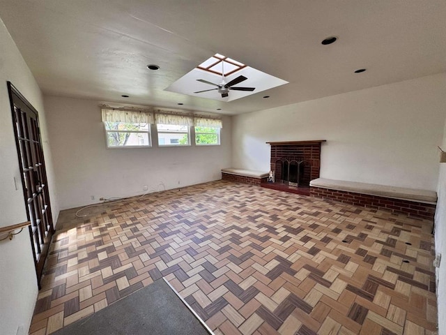 unfurnished living room with a fireplace, a skylight, and ceiling fan