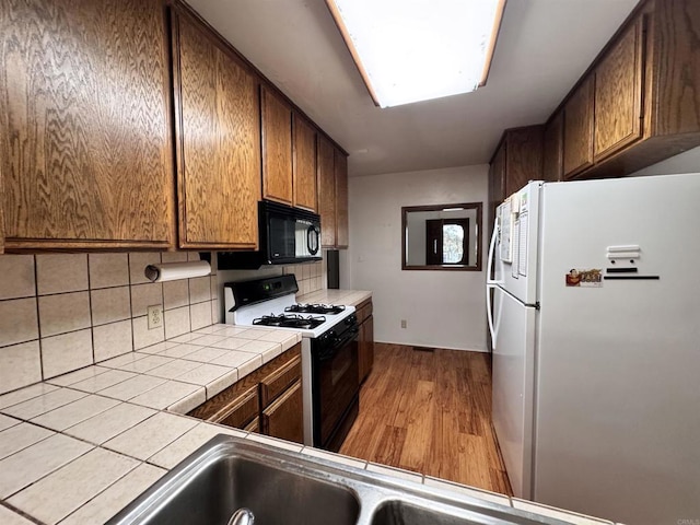 kitchen with black microwave, tile counters, freestanding refrigerator, wood finished floors, and gas range oven