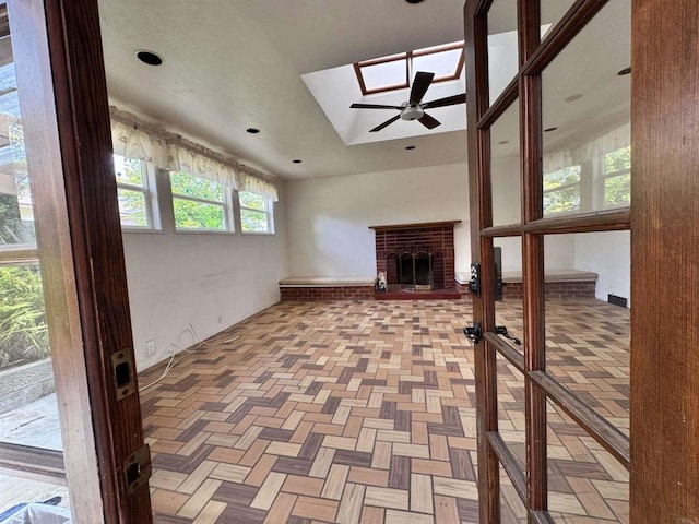 unfurnished living room with a skylight, a ceiling fan, and a brick fireplace