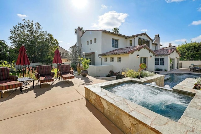 rear view of property featuring fence, a patio, stucco siding, a tiled roof, and an in ground hot tub