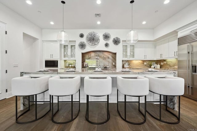 kitchen with visible vents, a breakfast bar, white cabinets, built in fridge, and backsplash