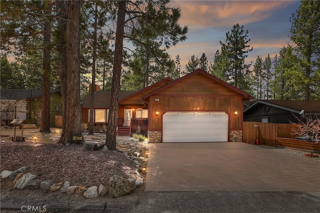 rustic home with a garage, fence, driveway, and stone siding