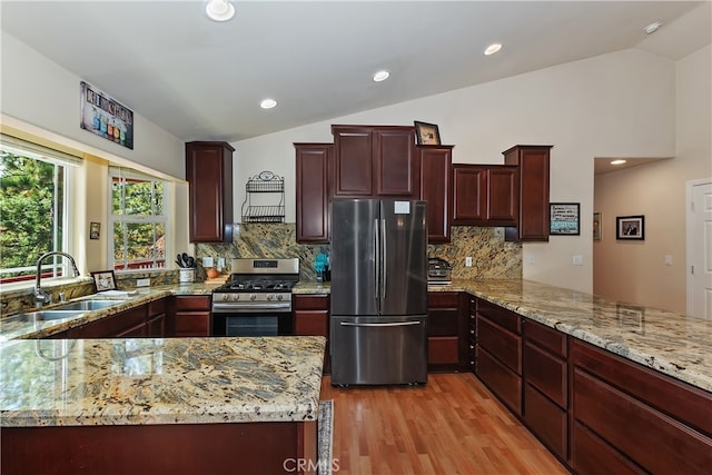 kitchen with appliances with stainless steel finishes, light stone countertops, light wood-type flooring, a sink, and lofted ceiling