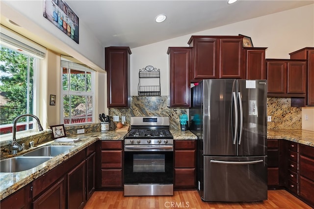 kitchen with a sink, light stone counters, reddish brown cabinets, stainless steel appliances, and light wood-style flooring