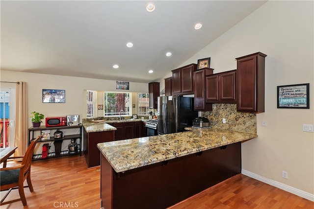 kitchen with stainless steel gas stove, light stone counters, freestanding refrigerator, a peninsula, and light wood-style floors