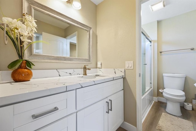 full bath with vanity, wood finished floors, toilet, baseboards, and enclosed tub / shower combo