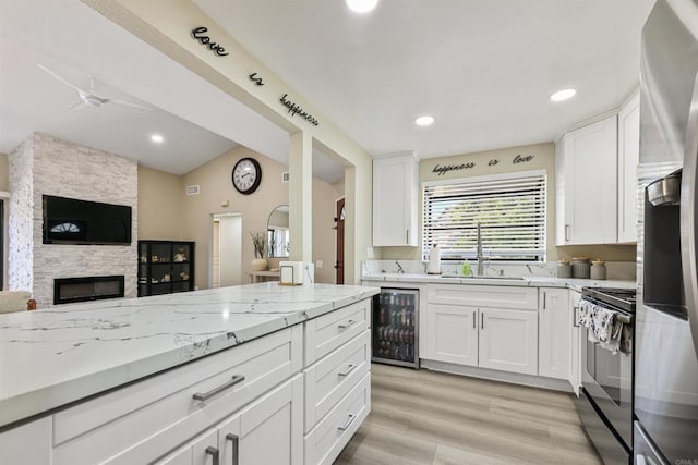 kitchen with a sink, beverage cooler, white cabinetry, open floor plan, and range with electric stovetop