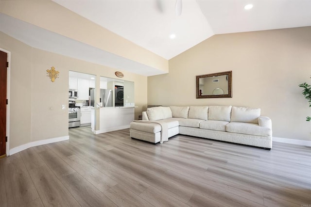 living area featuring baseboards, stacked washing maching and dryer, light wood-type flooring, recessed lighting, and vaulted ceiling