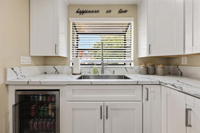 kitchen with white cabinets, beverage cooler, light stone countertops, and a sink