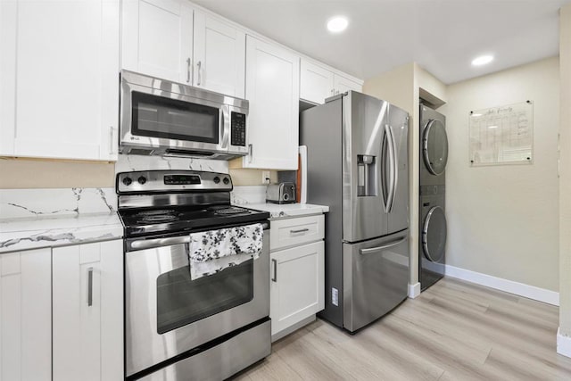 kitchen with stacked washer / dryer, baseboards, white cabinetry, light wood finished floors, and appliances with stainless steel finishes