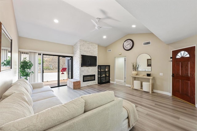 living room featuring a ceiling fan, a stone fireplace, visible vents, baseboards, and light wood-style flooring