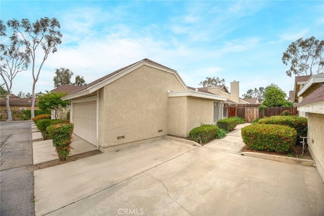 view of home's exterior with crawl space, driveway, fence, an attached garage, and stucco siding