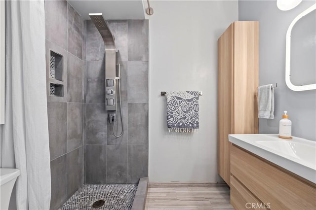 full bathroom with vanity, wood finished floors, a tile shower, and toilet