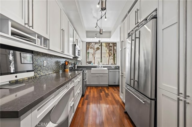kitchen with decorative backsplash, a sink, dark stone counters, stainless steel appliances, and dark wood-type flooring